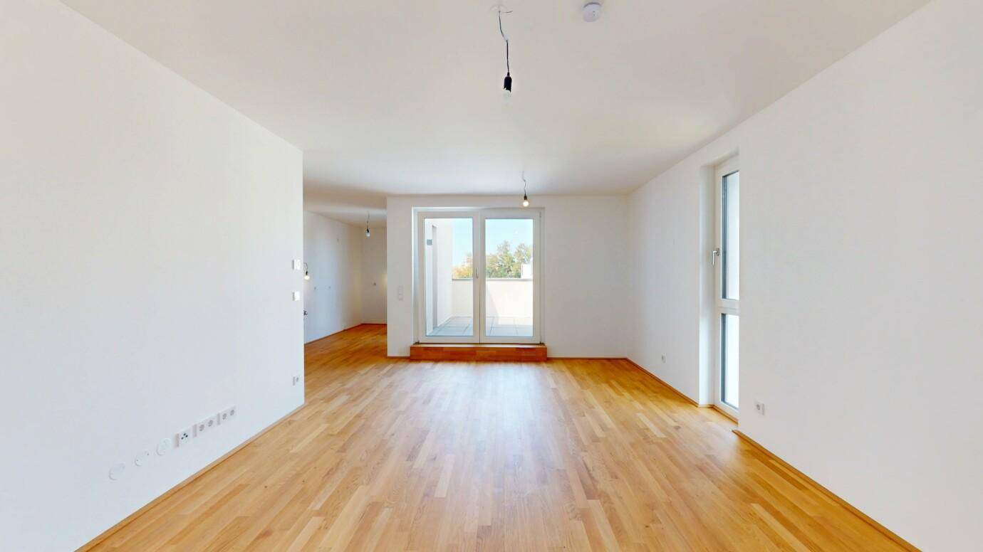 Heller, leerer Wohnraum mit Parkettboden und Zugang zur Terrasse.