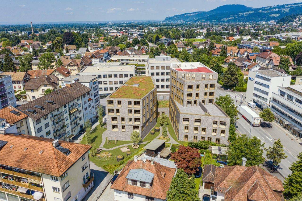 Eine Vogelperspektive zeigt zwei moderne Gebäude mit begrünten Dächern und einem Spielplatz in einer städtischen Umgebung in Dornbirn (Konfigurator, Eigentumswohnung, Zentrum).
