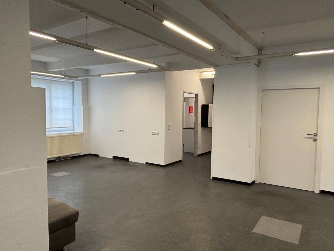 Großer, offener Gewerberaum mit mehreren Fenstern und funktionaler Deckenbeleuchtung.