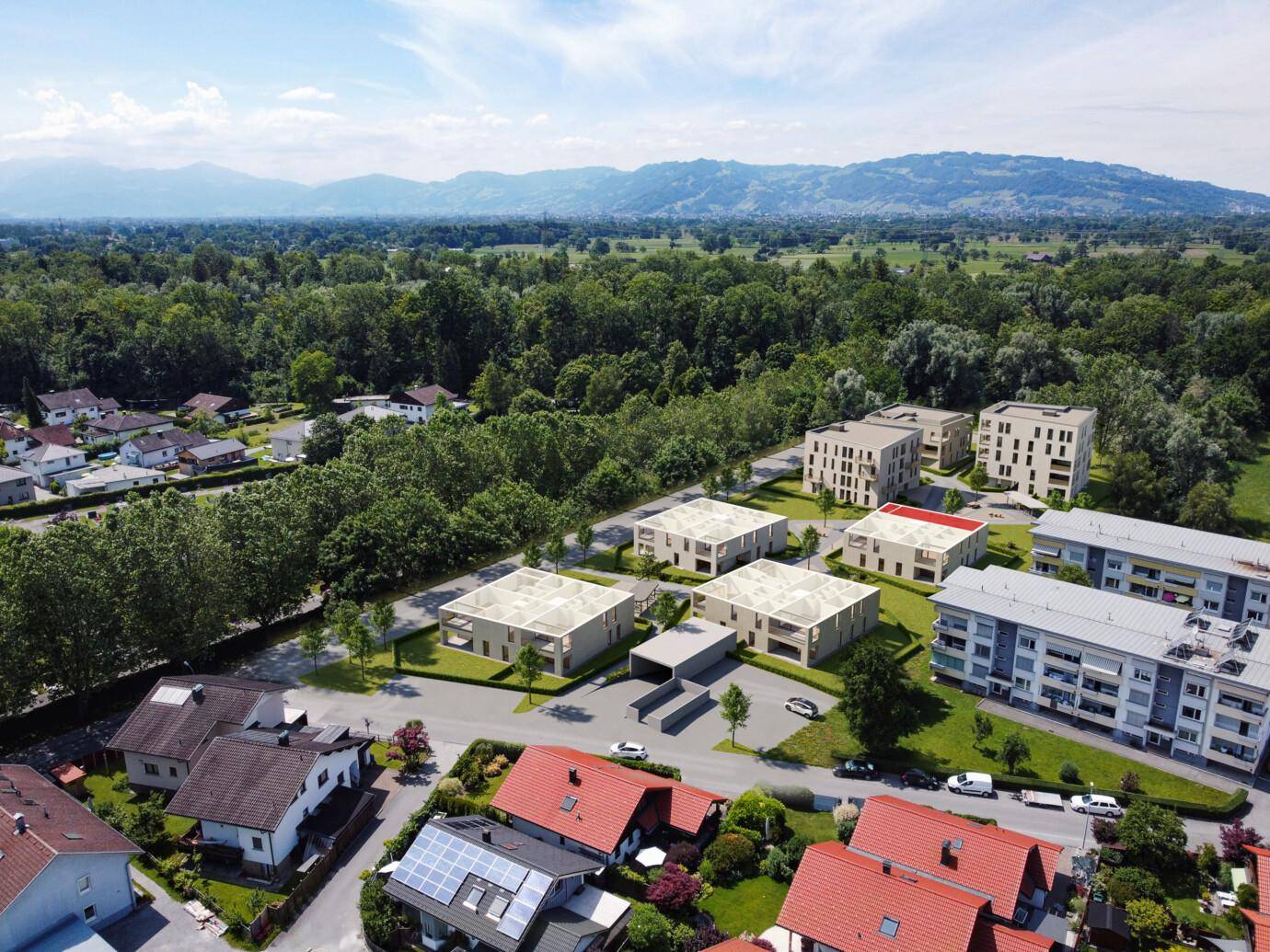 Vogelperspektive auf ein Modell von Neubauten mit hellen Fassaden und roten Dächern in einer grünen Landschaft mit Bergen am Horizont.
