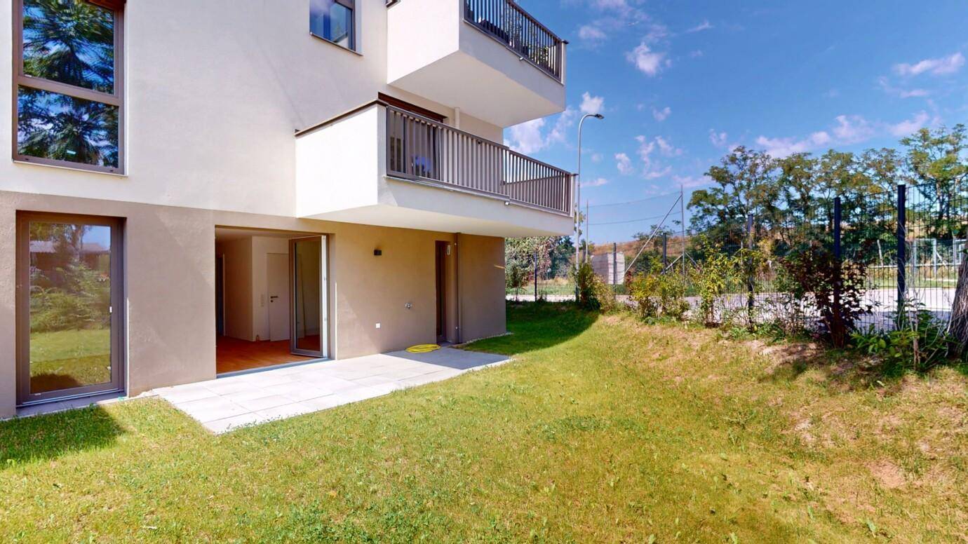 Außenbereich des Neubaus mit Rasenfläche, Terrasse und Balkonen.
