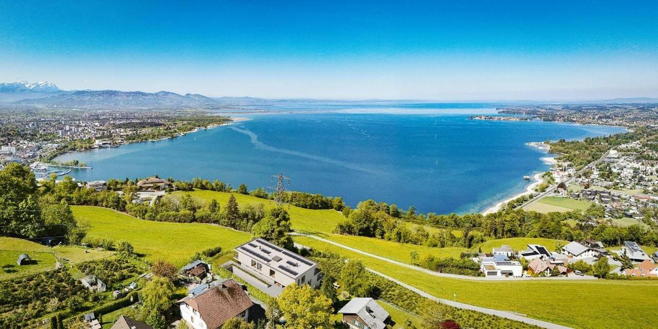 Weitläufige Luftaufnahme mit Blick auf den See, die umliegende Landschaft und die Wohnanlage.
