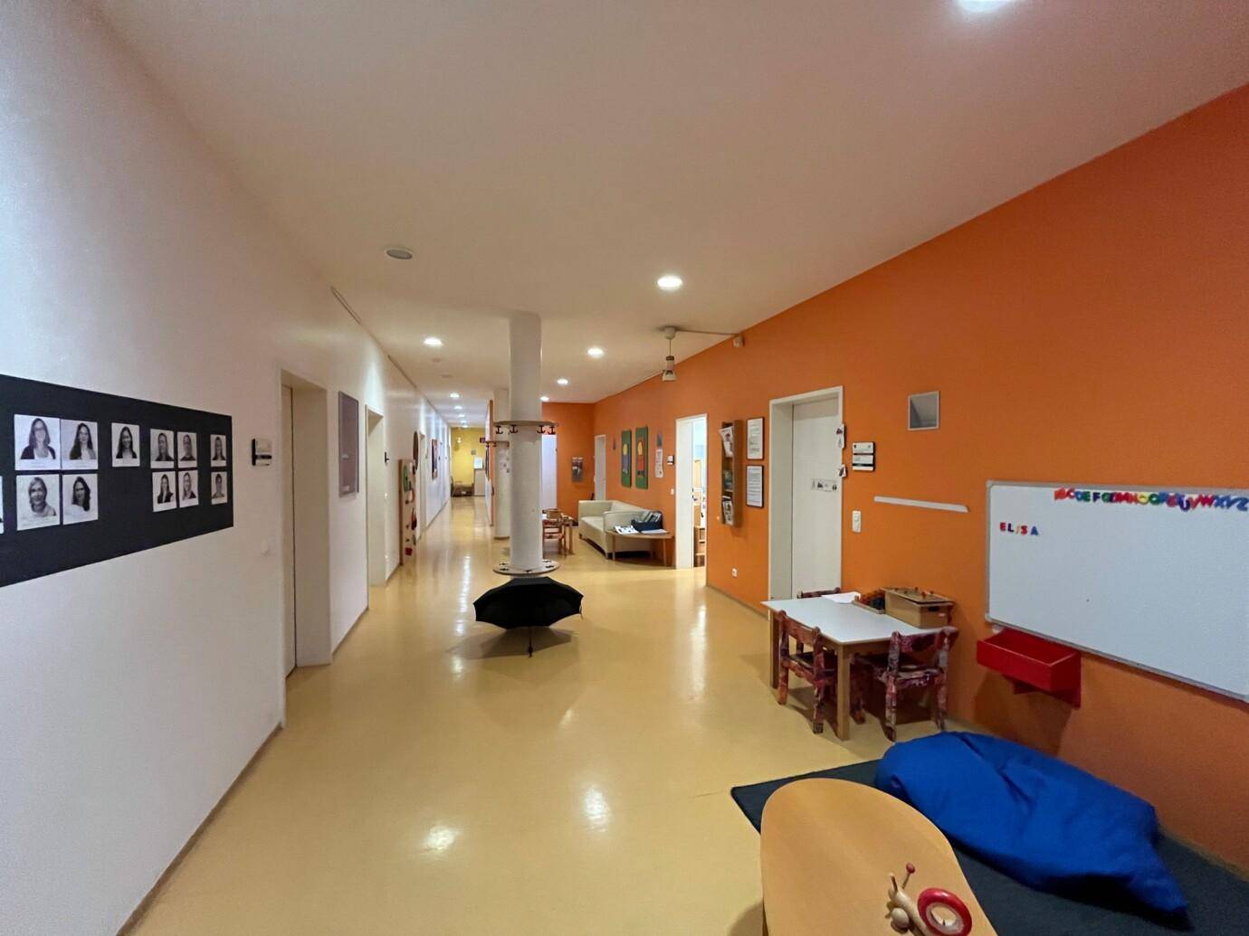 Langer Flur mit leuchtend orangefarbenen Wänden, gelbem Boden und verschiedenen Kindermöbeln und Dekorationen.