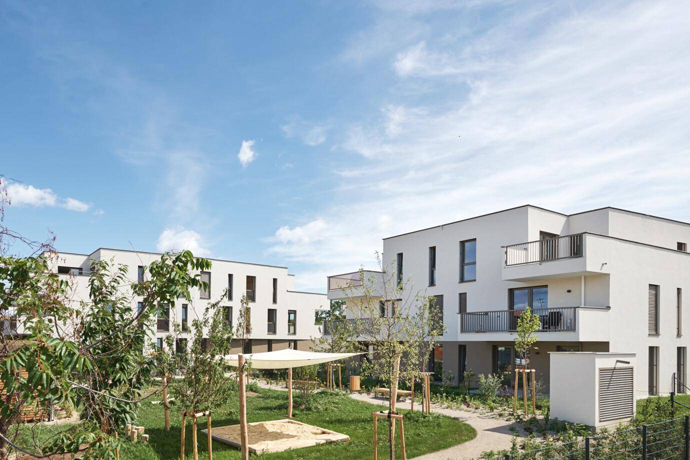 Moderne Wohngebäude umgeben von einer grünen Gemeinschaftsanlage mit Sandkasten.