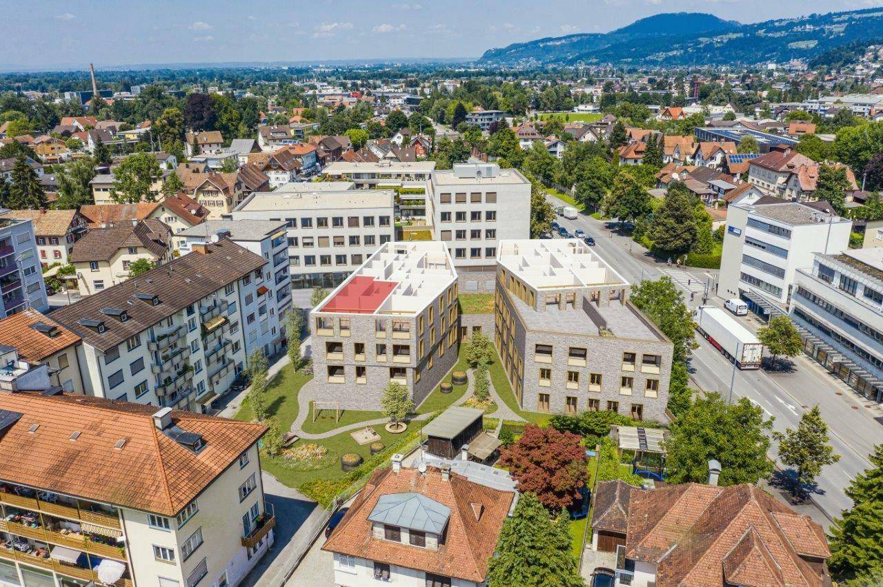 Luftaufnahme von modernen Wohngebäuden mit einem grünen Innenhof, umgeben von weiteren Gebäuden und einer Straße in Dornbirn (Konfigurator, Eigentumswohnung, Zentrum).