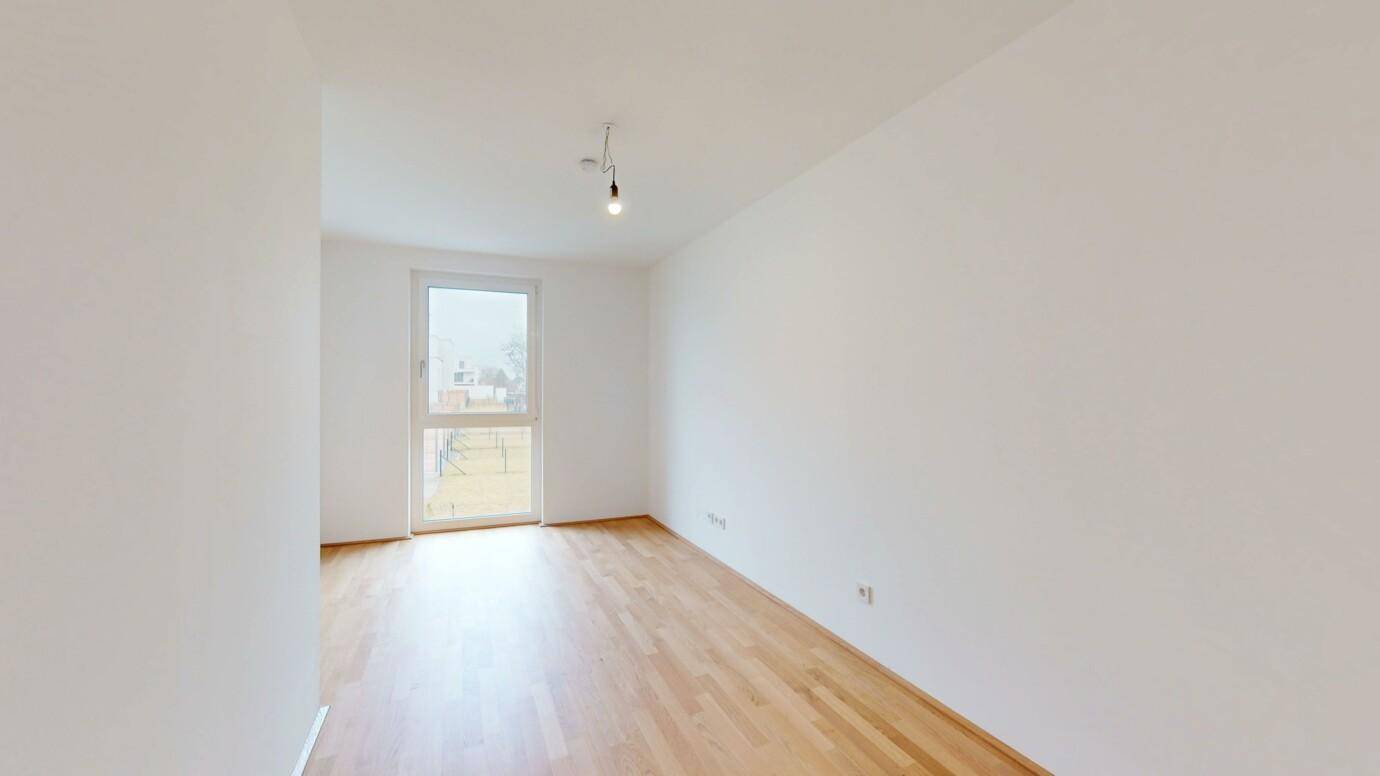 Leeres Zimmer mit Holzboden und Fenster, bietet viel natürliches Licht.