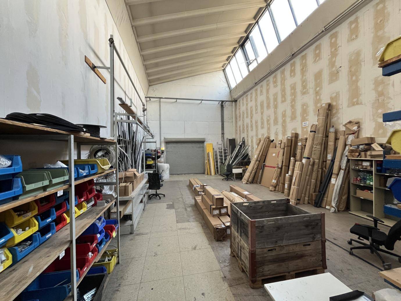 Geräumige Lagerhalle mit hohen Decken, Oberlichtern und verschiedenen Materialien auf Regalen und dem Boden.