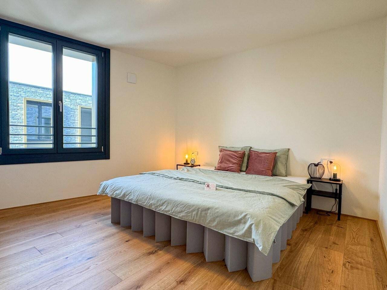 Schlafzimmer mit Holzboden, großen Fenstern und schlichter, moderner Einrichtung.