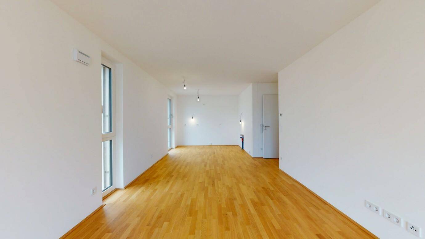 Geräumiges, helles Wohnzimmer mit Holzboden und mehreren großen Fenstern.