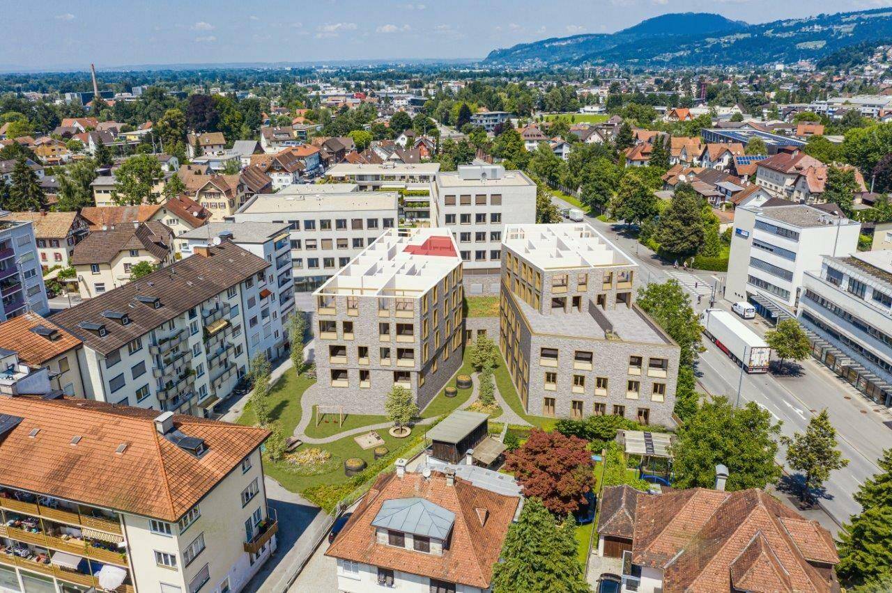 Luftaufnahme eines modernen Wohnkomplexes in städtischer Umgebung mit viel Grün und Bergblick.