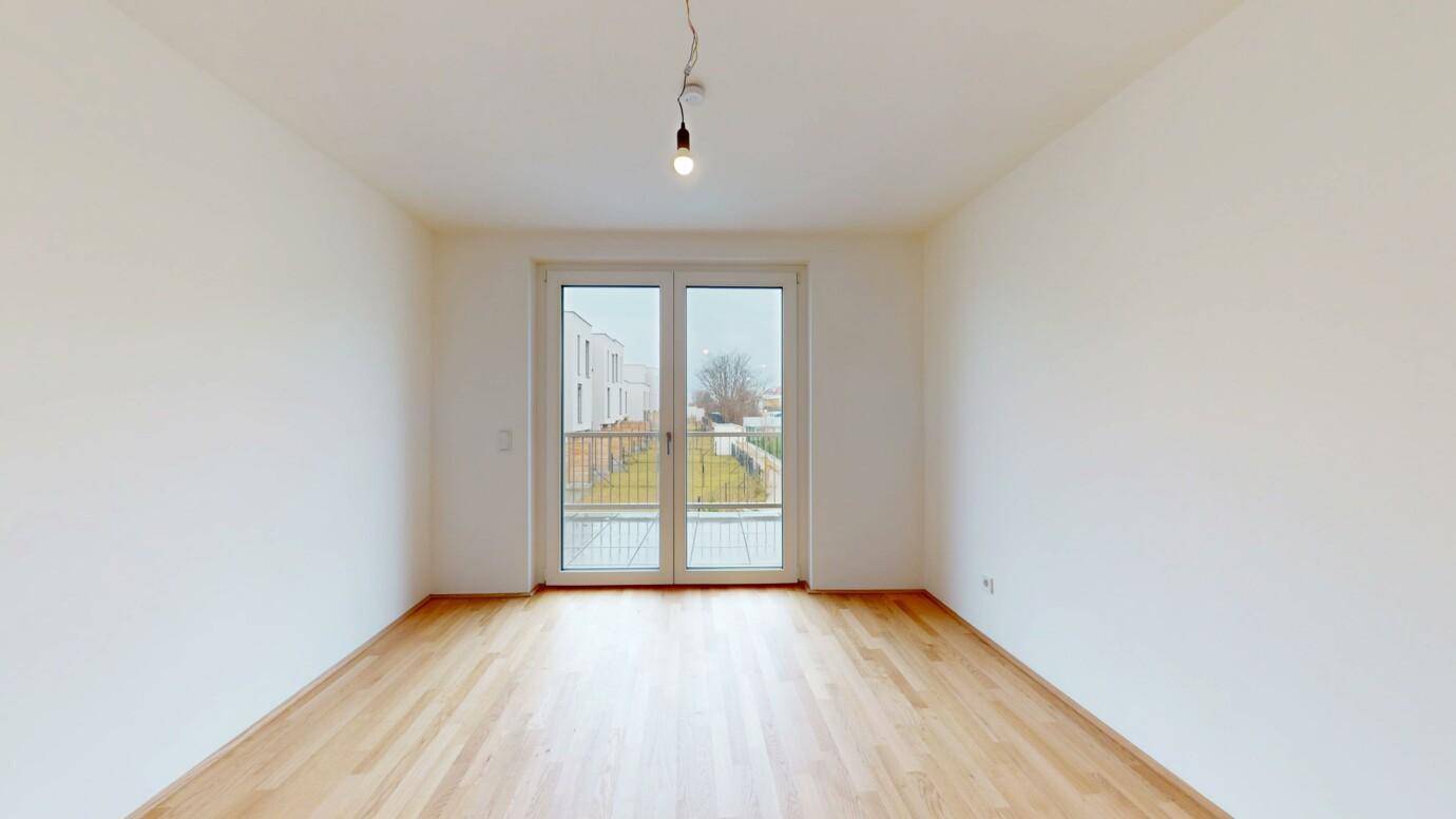 Leeres Schlafzimmer mit hellem Holzboden und großem Fenster mit Blick nach draußen.