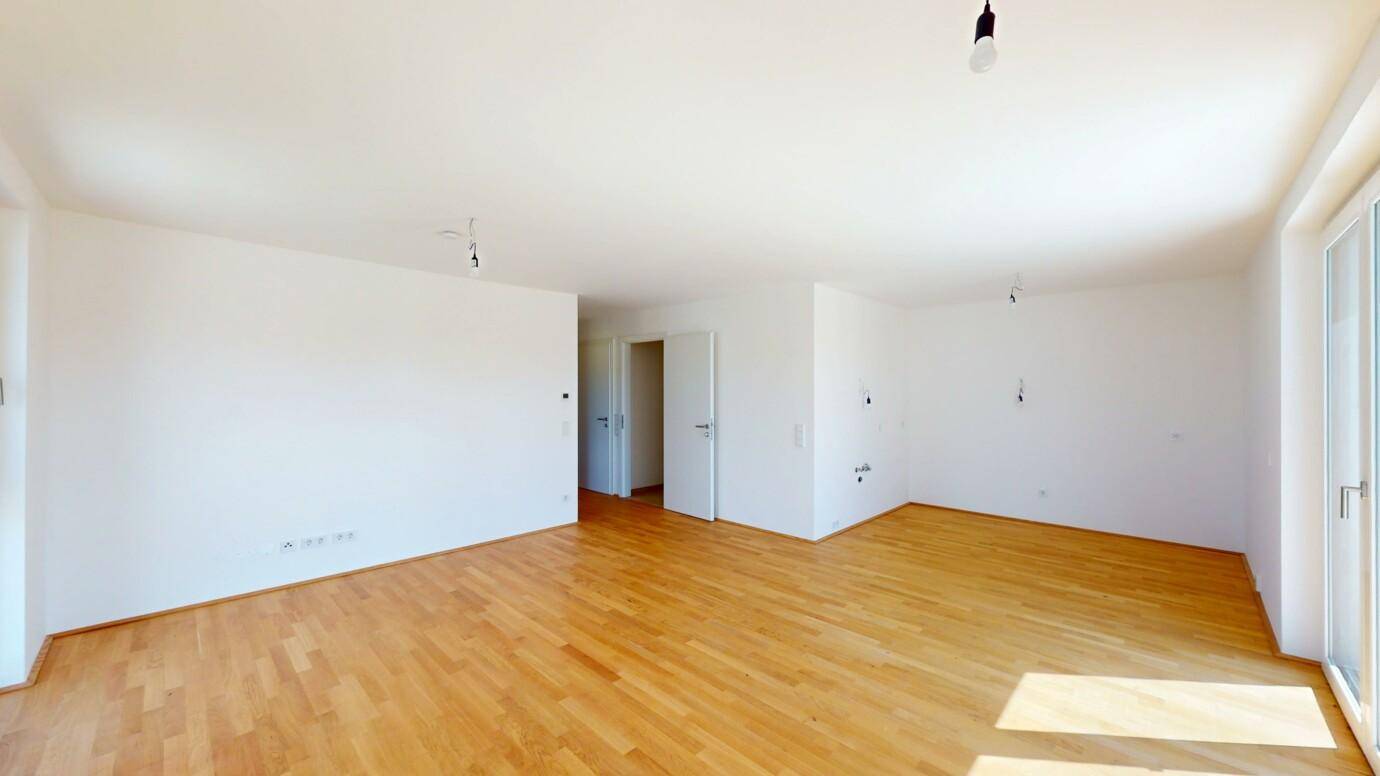Geräumiges Wohnzimmer mit hellem Parkettboden und weißen Wänden, bereit zur Einrichtung.