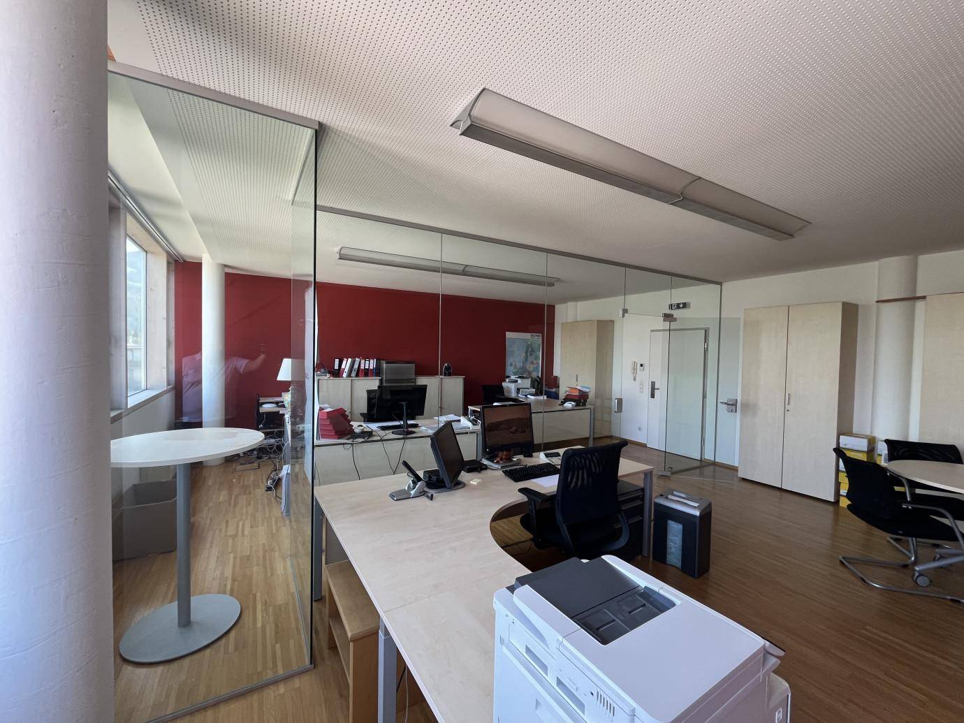 Geräumiges Büro mit Glaswänden, modernen Arbeitsplätzen und Holzboden.