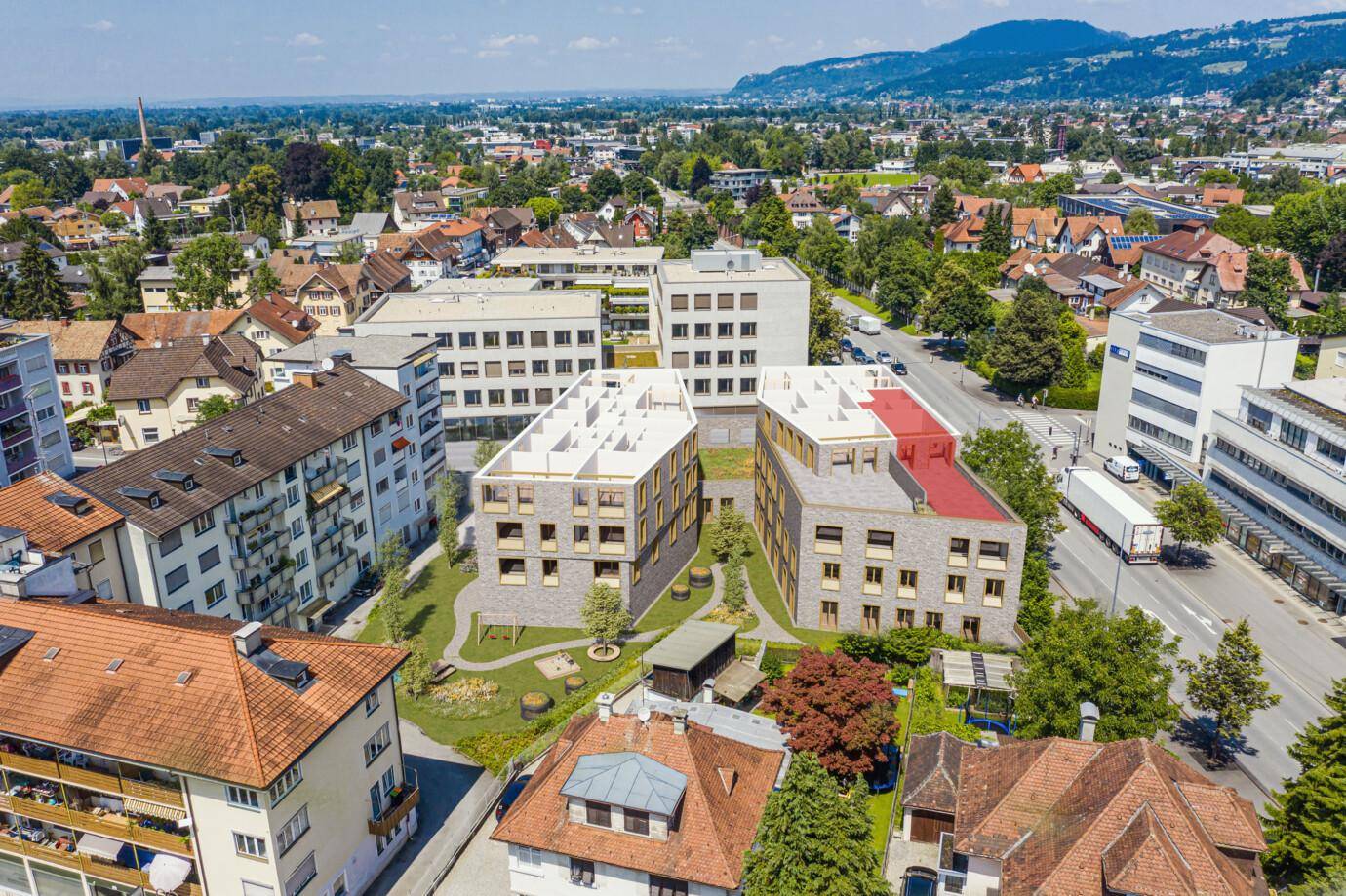 Luftaufnahme eines modernen Wohnkomplexes mit umliegender Bebauung, Grünflächen und Bergblick in einer städtischen Umgebung.