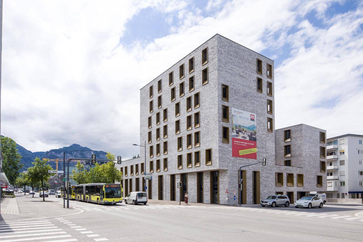 Gesamtansicht des modernen Wohnkomplexes an einer belebten Straße mit öffentlichem Nahverkehr.