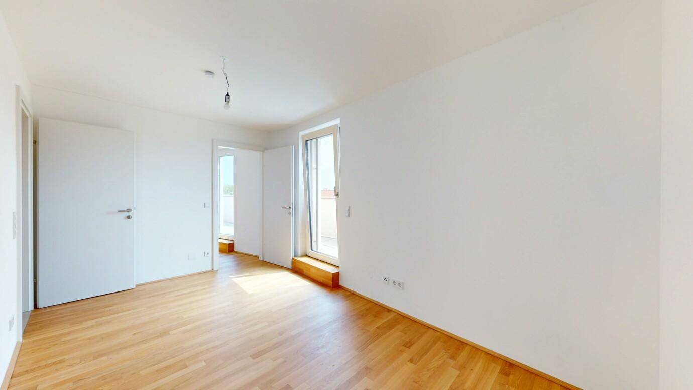 Helles Zimmer mit Parkettboden und Zugang zu einem Balkon oder einer Terrasse.
