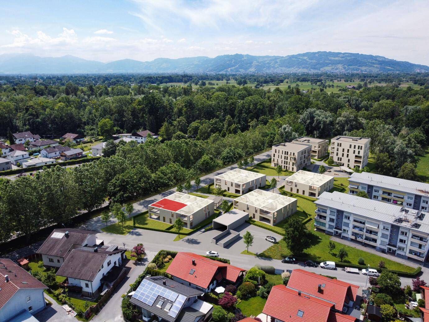 Luftaufnahme einer Wohnsiedlung mit modernen Gebäuden, umgeben von Natur und Bergen.