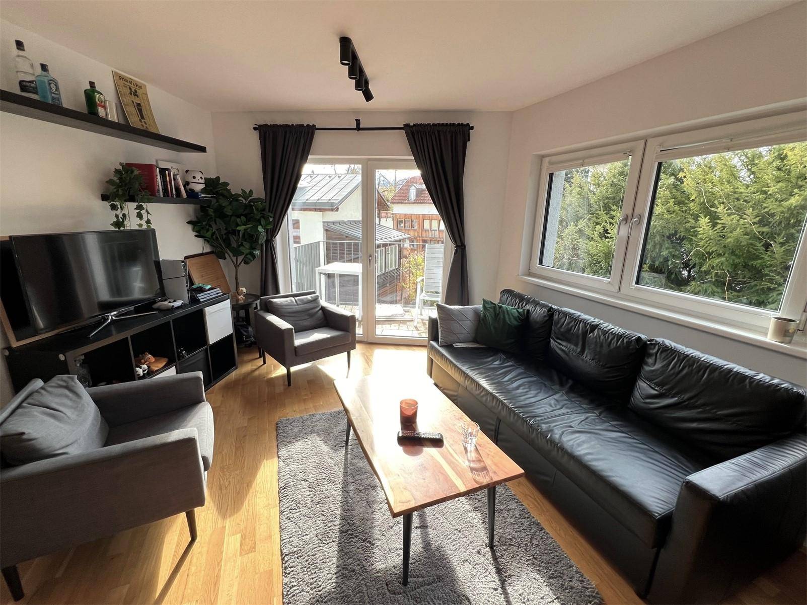 Heller Wohnbereich mit Ledersofa, Sesseln und Zugang zum Balkon, ausgestattet mit Holzboden.