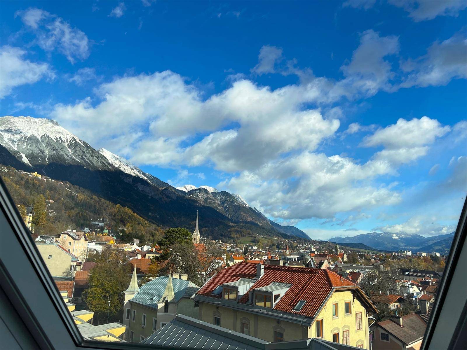 Atemberaubender Blick aus einem Dachfenster auf die schneebedeckten Berge und die Stadtlandschaft.