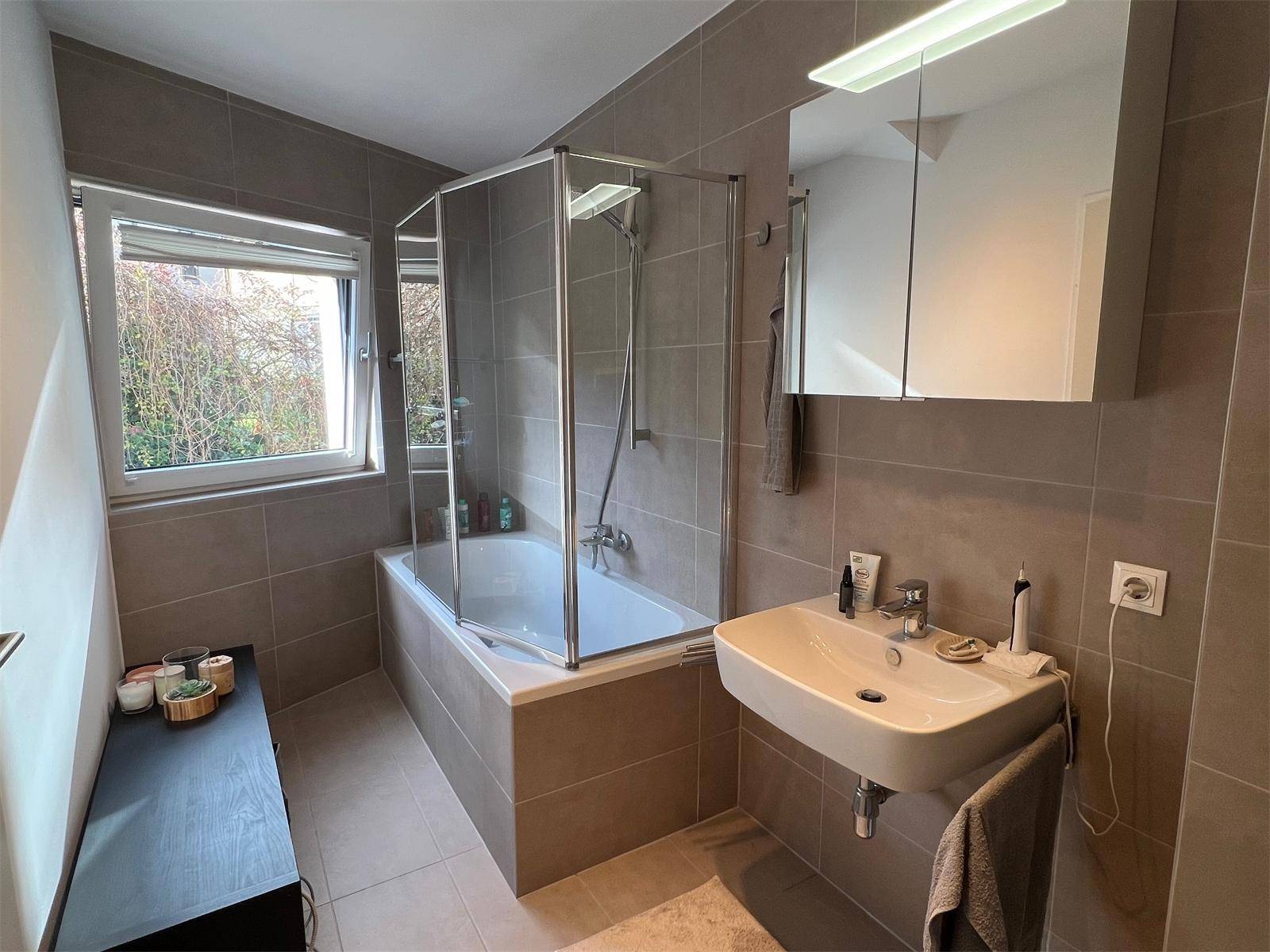Modernes Badezimmer mit Badewanne, Duschabtrennung, Waschbecken und Fenster für Tageslicht.