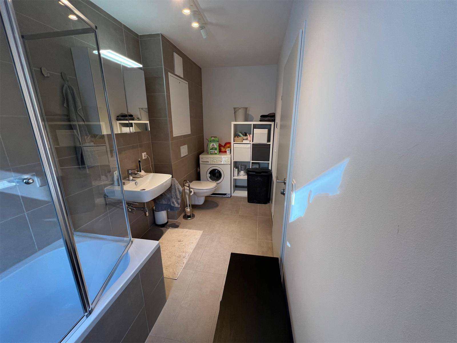 Funktionales Badezimmer mit Badewanne, Toilette und Platz für eine Waschmaschine.