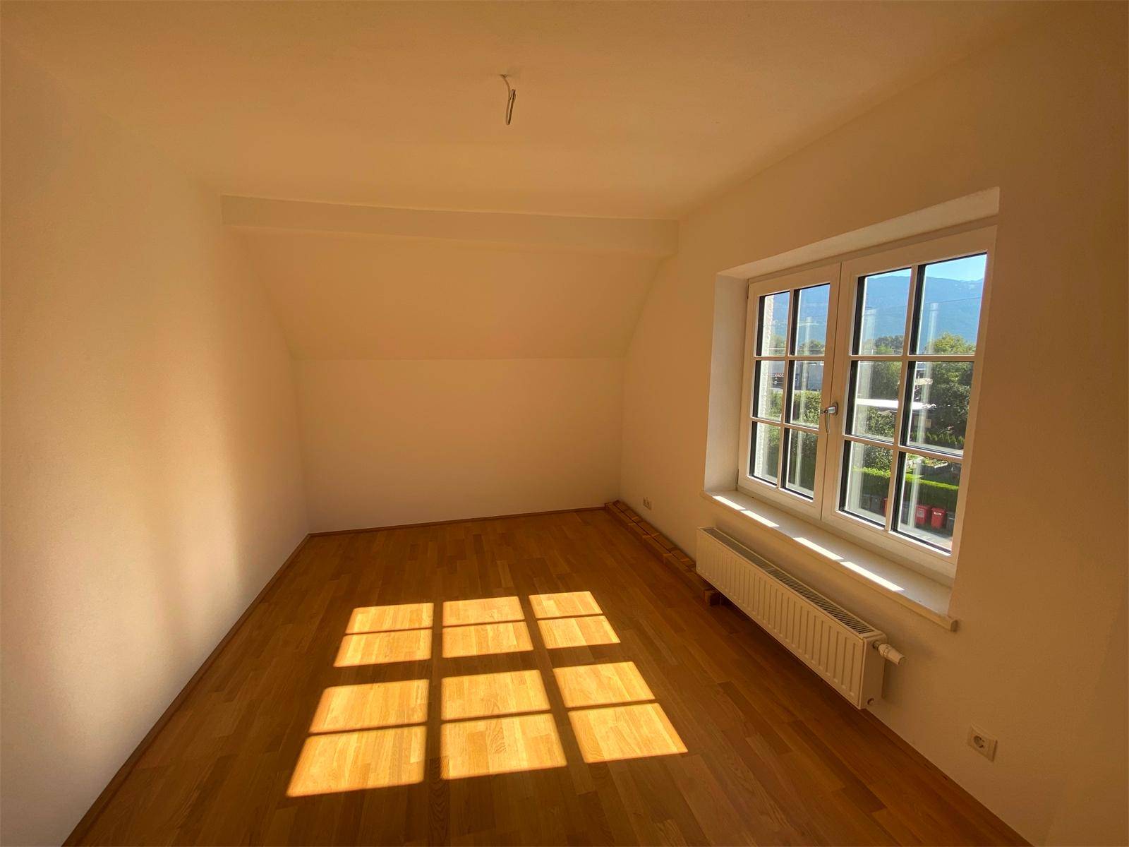 Helles Schlafzimmer mit Parkettboden, großem Fenster und viel natürlichem Sonnenlicht.