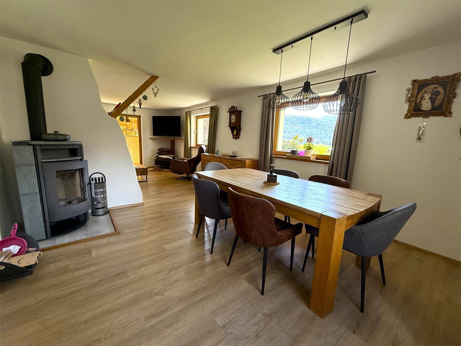 Gemütlicher Essbereich mit Holztisch, Kaminofen und weitem Blick auf die grüne Landschaft.