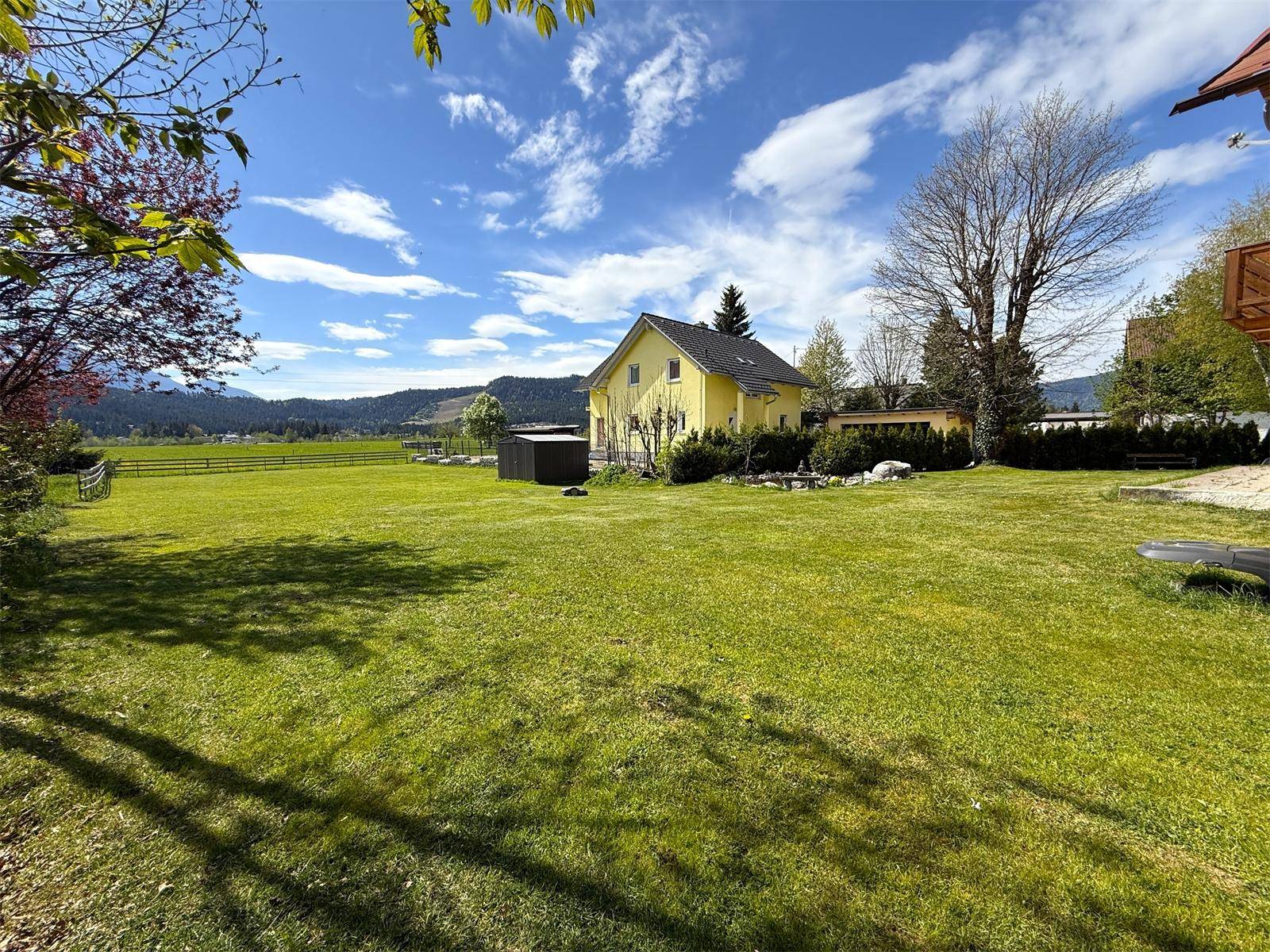Weitläufiger grüner Garten mit dem Wohnhaus im Hintergrund und Blick auf die umliegende Landschaft.