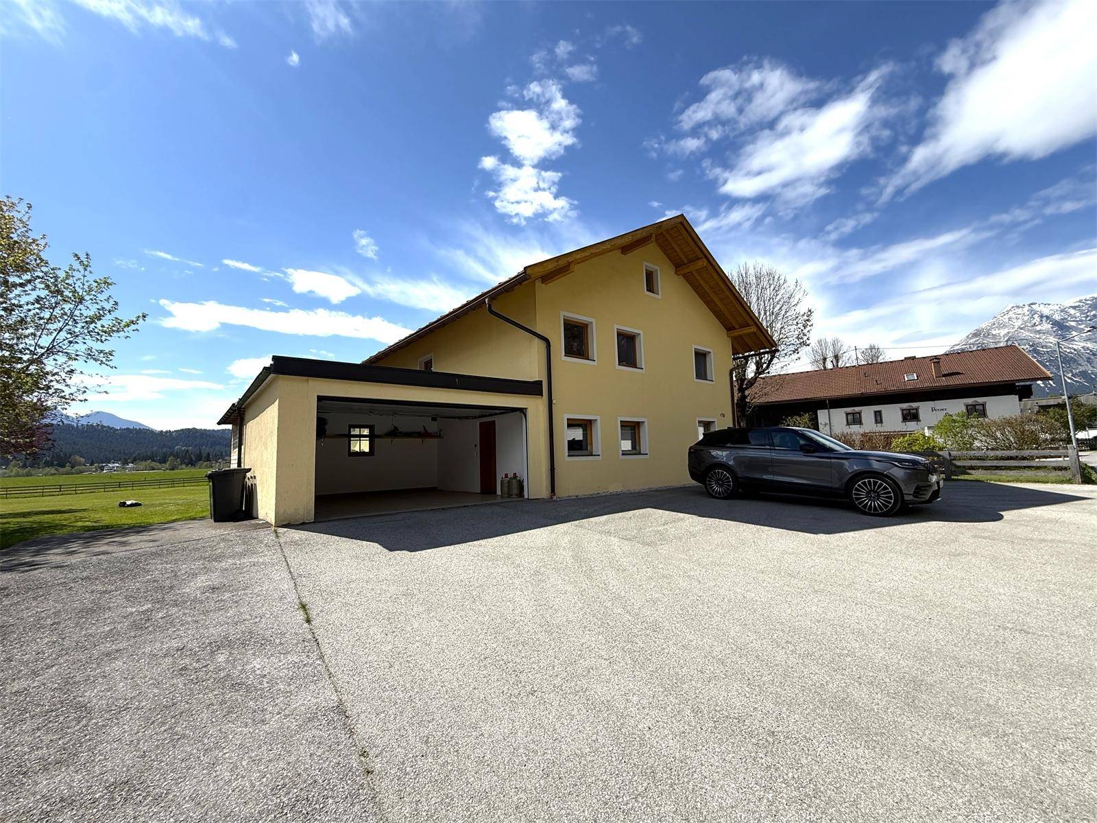 Gelbes Wohnhaus mit integrierter Garage und großem Vorplatz, umgeben von ländlicher Landschaft.