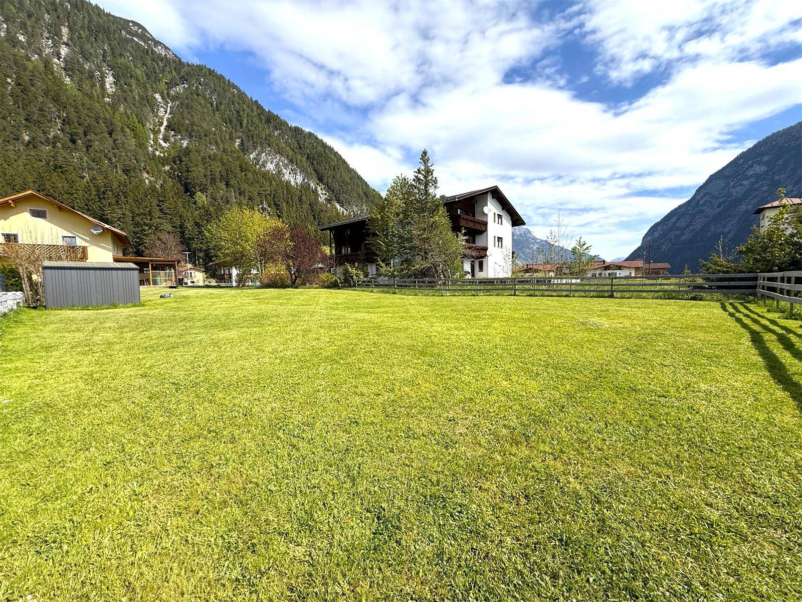 Große, gepflegte Rasenfläche mit Blick auf benachbarte Häuser und die majestätische Berglandschaft.