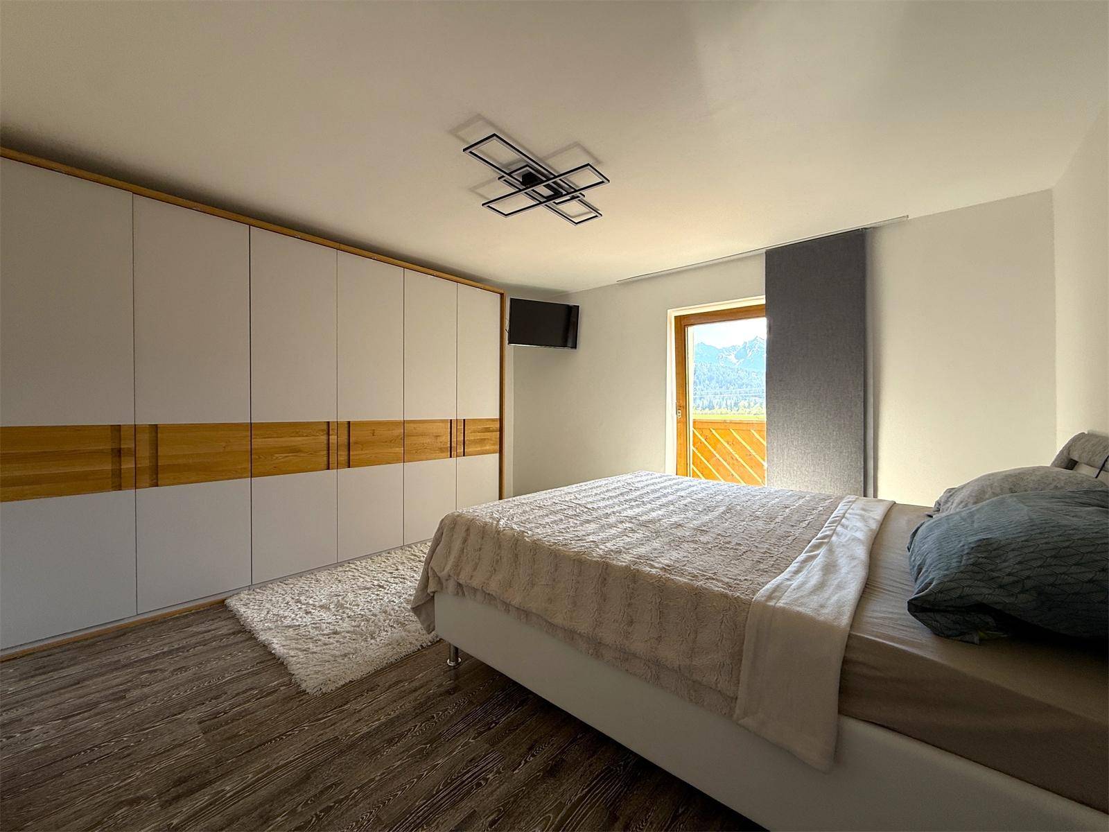 Schlafzimmer mit großem Einbauschrank, Doppelbett und Zugang zu einem Balkon mit Bergblick.