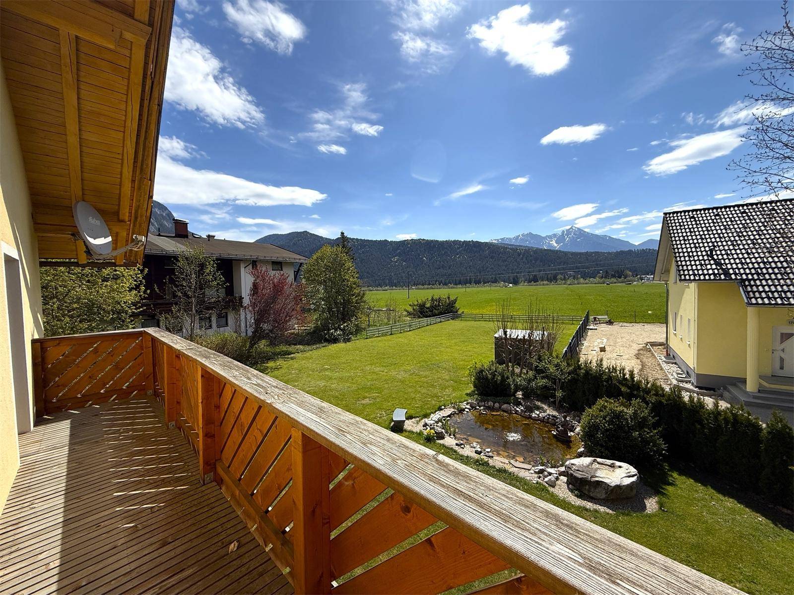 Geräumiger Holzbalkon mit weitem Blick über den Garten, Teich und die umliegende Berglandschaft.