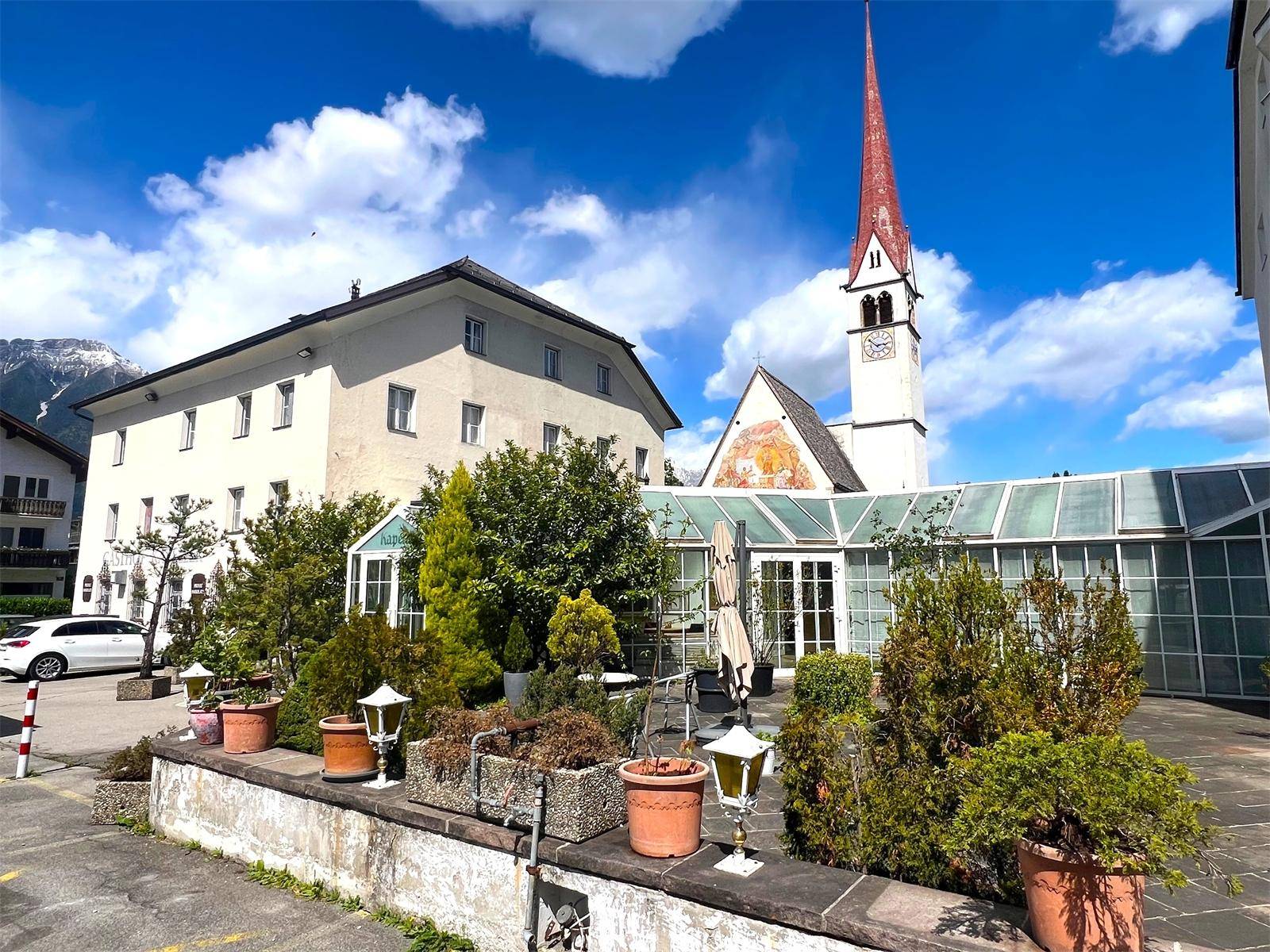Historisches Gebäude mit angrenzendem Wintergarten und einem Kirchturm im Hintergrund.