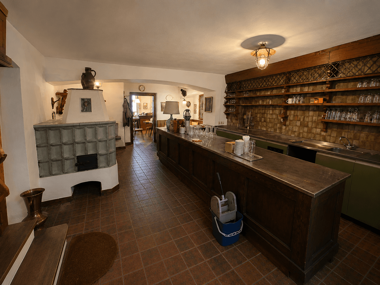 Rustikale Bar mit Kachelofen, Holztheke und Regalen für Gläser und Flaschen.