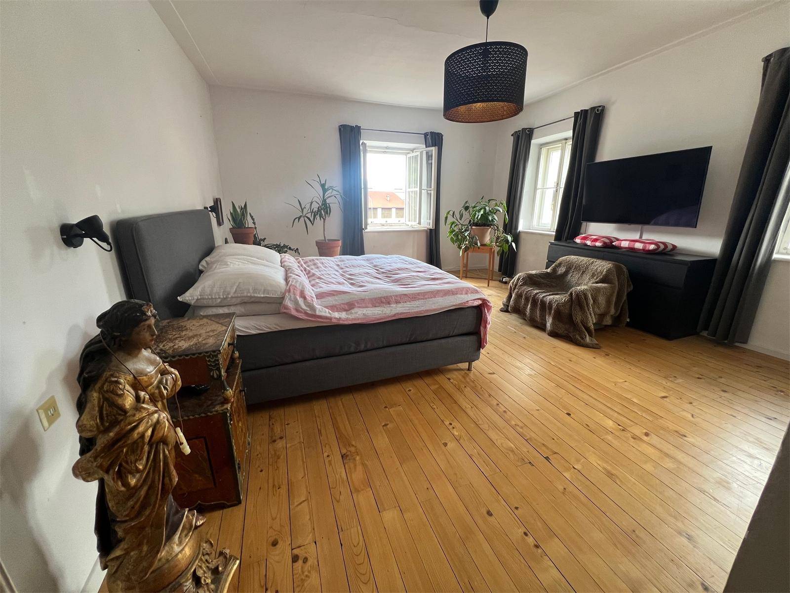 Schlafzimmer mit Holzdielenboden, Doppelbett und einem Fenster für natürliches Licht.