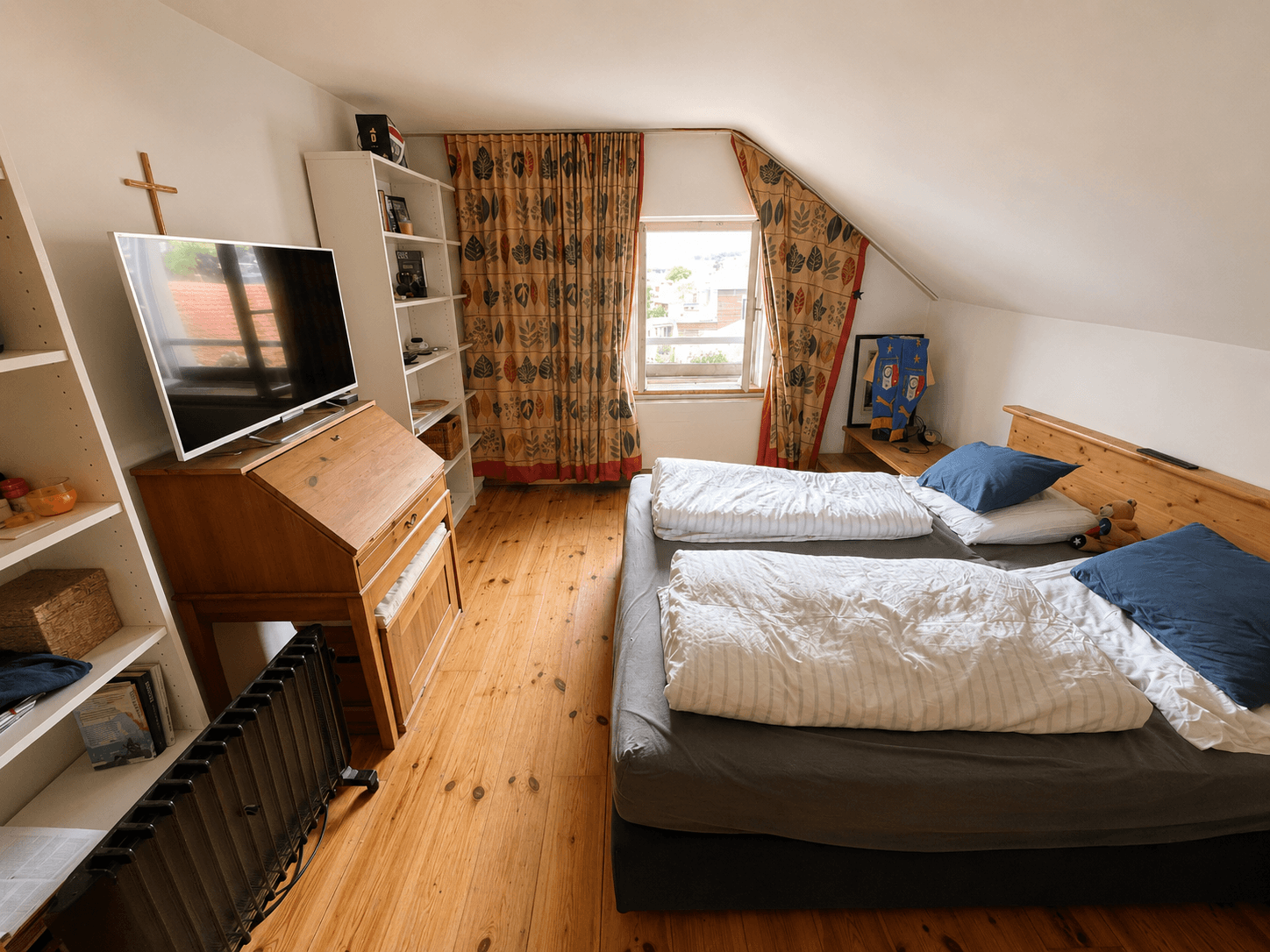 Schlafzimmer unter Dachschrägen mit Holzdielenboden, Doppelbett und Fenster.