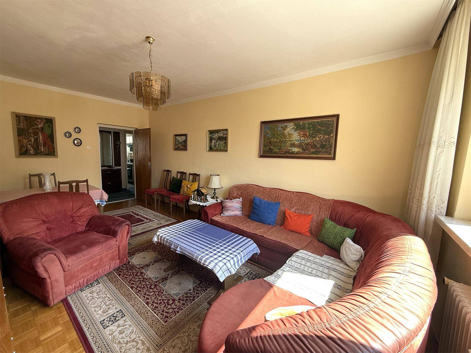 Gemütliches Wohnzimmer mit rotem Sofa, Sessel, Couchtisch und einem traditionellen Teppich.