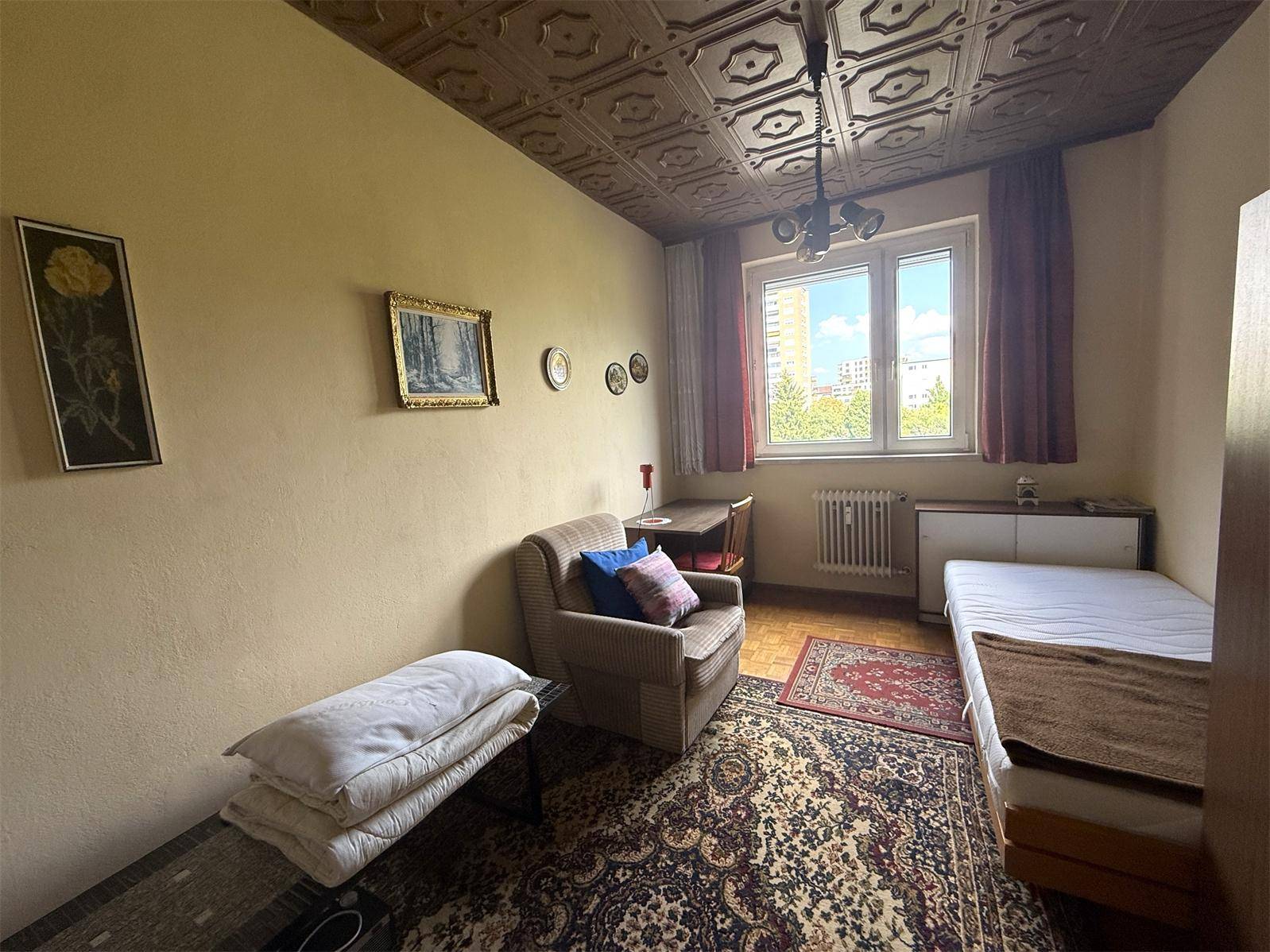 Zimmer mit Einzelbett, Sessel, Schreibtisch und einer auffälligen Deckenverkleidung.