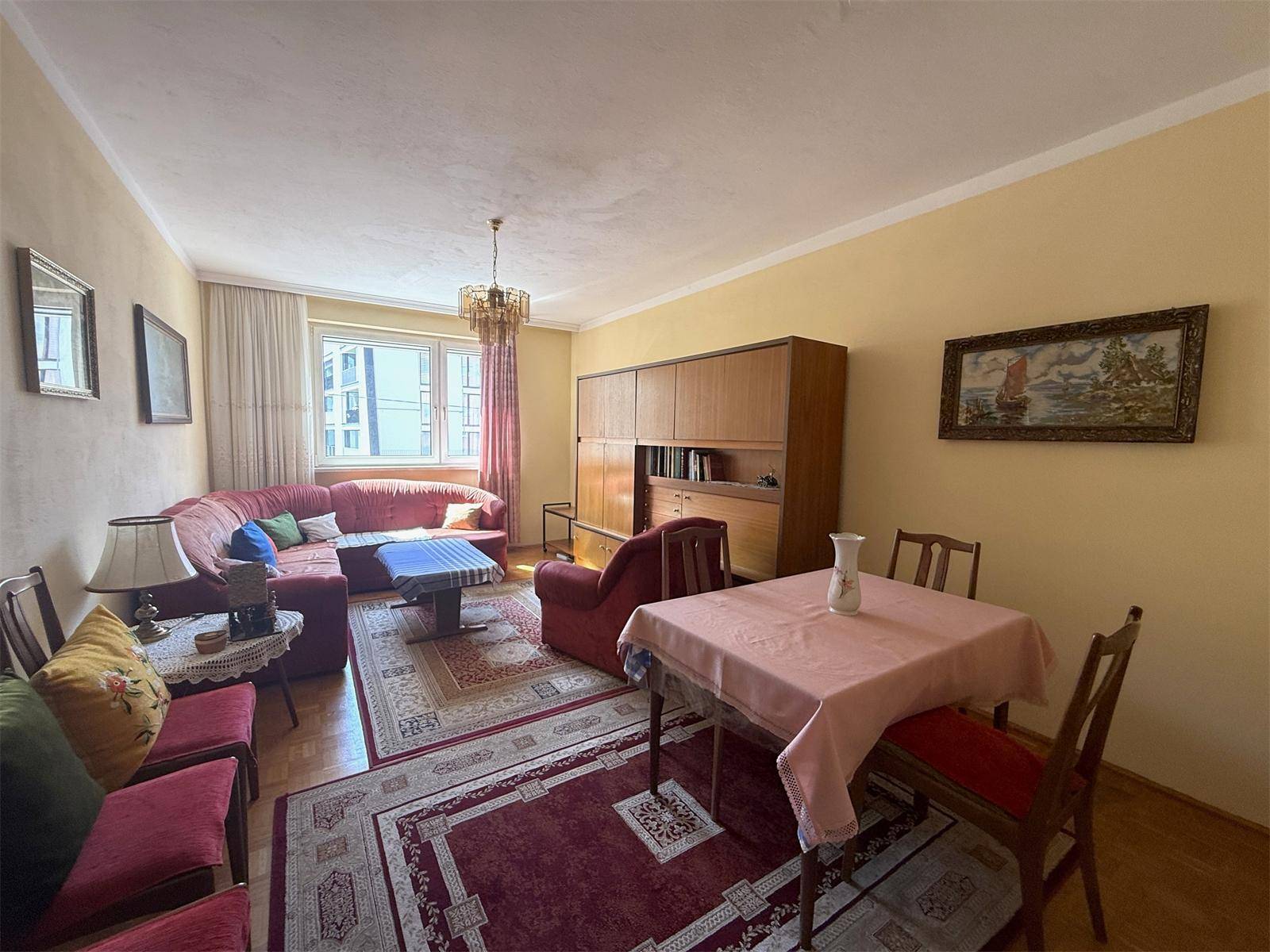 Wohn- und Essbereich mit rotem Sofa, Esstisch und einem großen Fenster für viel Licht.