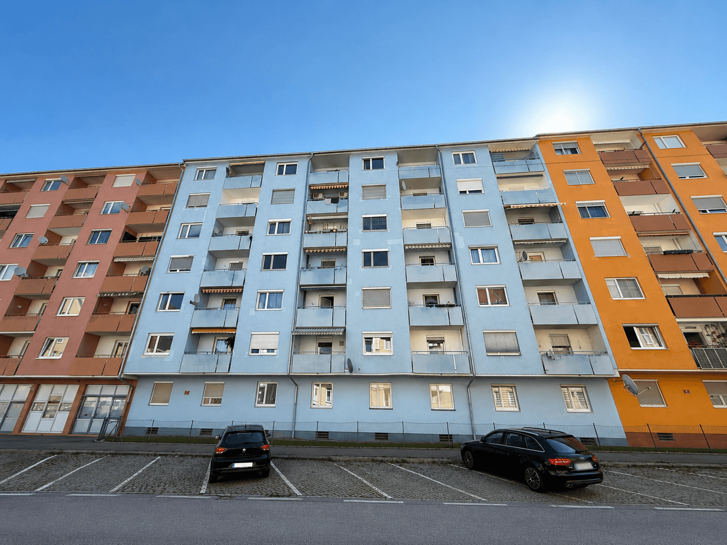 Fassade der Wohngebäude mit zahlreichen Balkonen und geparkten Autos davor.