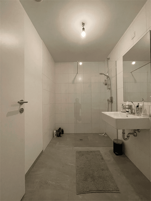 Modernes Badezimmer mit ebenerdiger Dusche, Waschbecken und hellen Fliesen an Wänden und Boden.