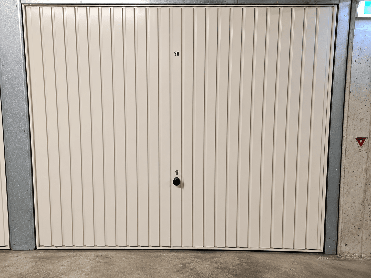 Einzelne Garagenbox mit weißem Rolltor und Nummer 98 in einer Tiefgarage.