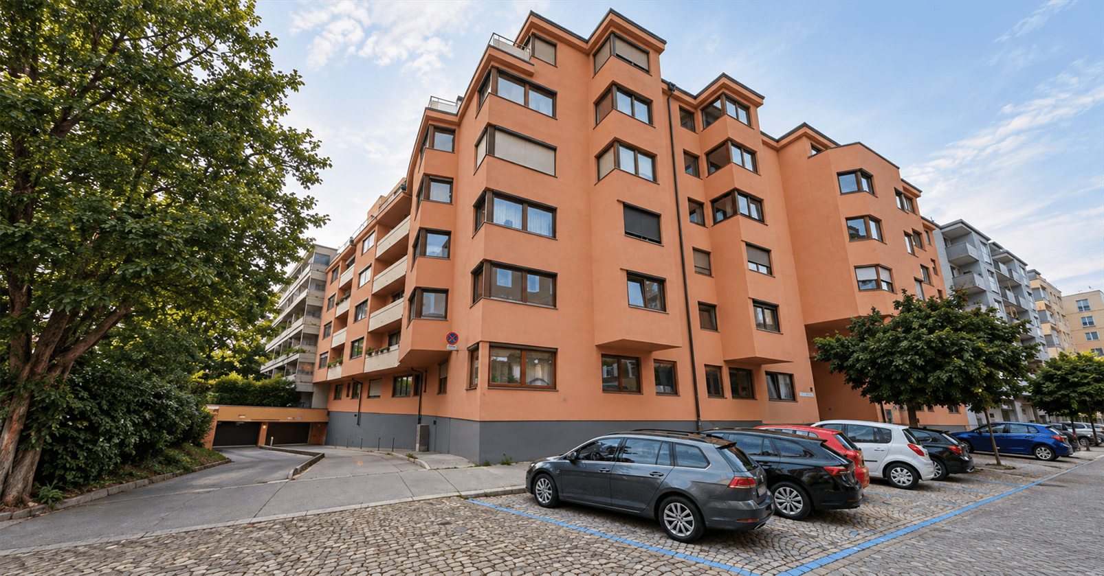 Modernes Wohngebäude mit orangefarbener Fassade, Balkonen und Außenparkplätzen.