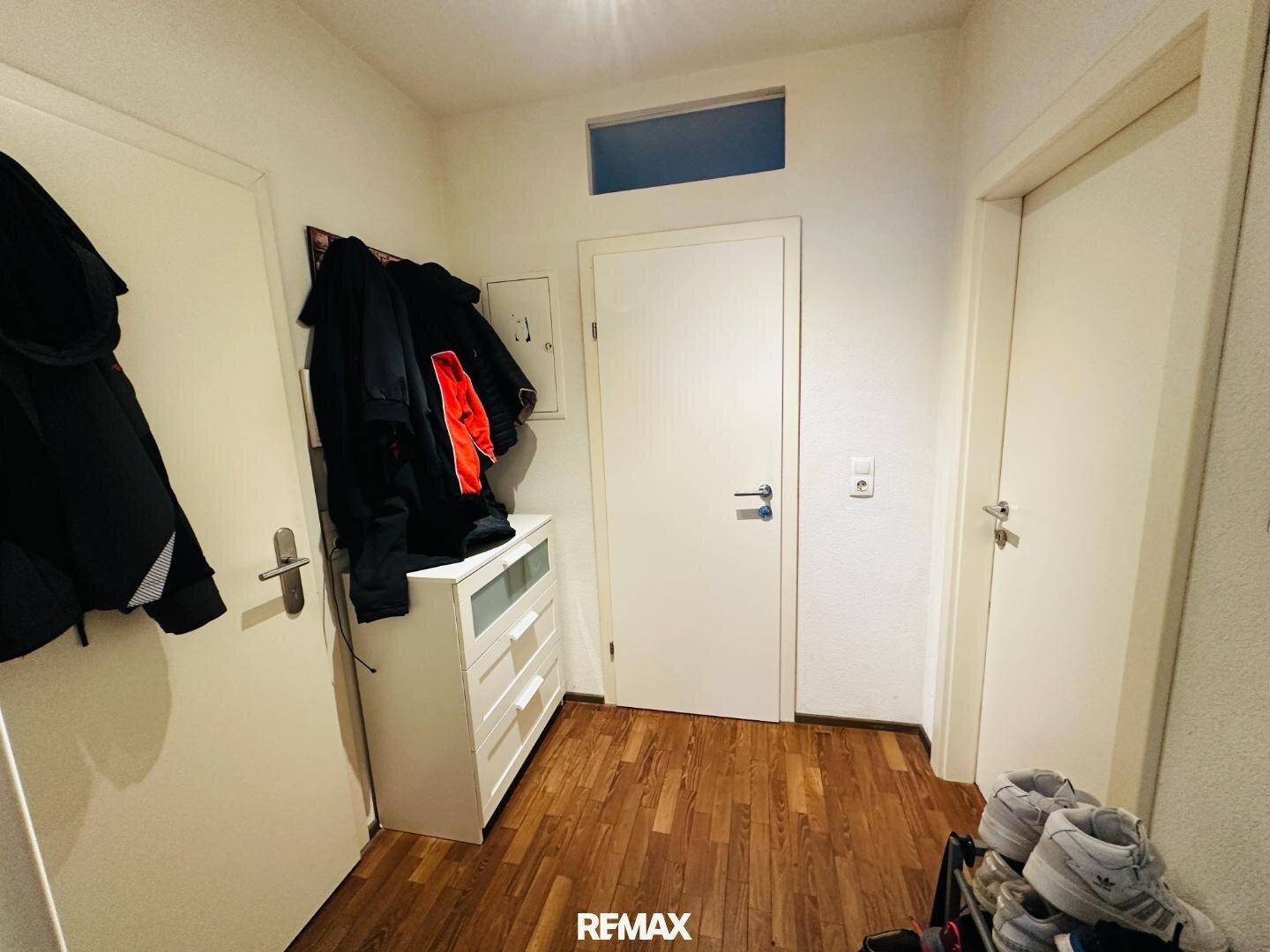 Eingangsbereich mit Holzparkettboden, Garderobe und weißen Türen, hell durch Oberlicht.