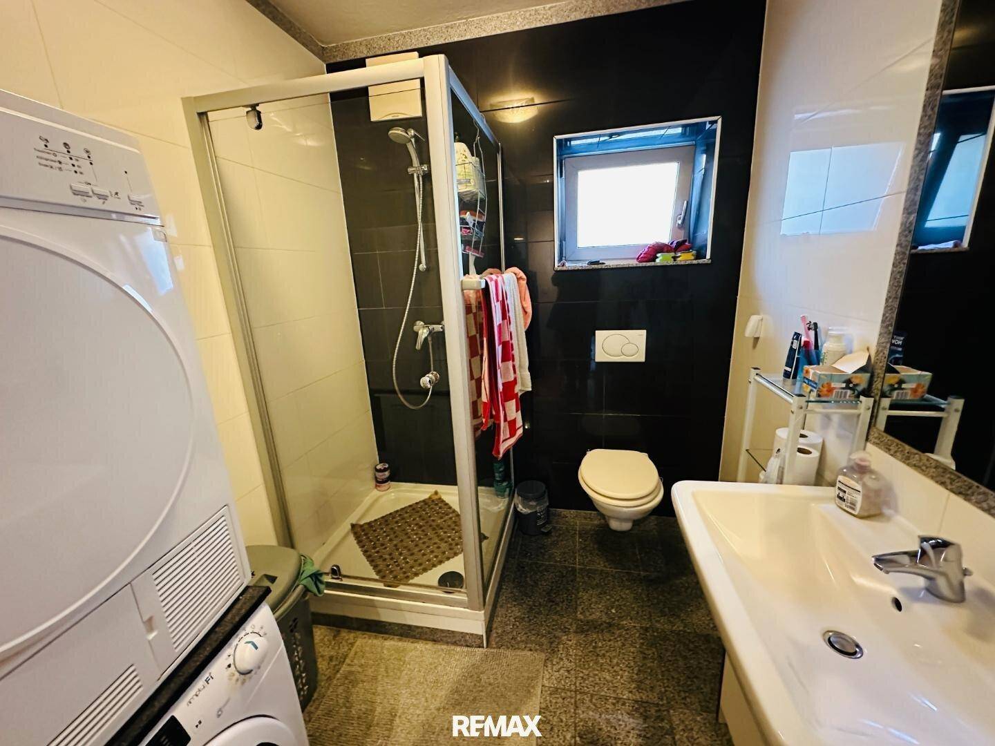 Funktionales Badezimmer mit Duschkabine, Toilette, Waschbecken und Waschmaschine.