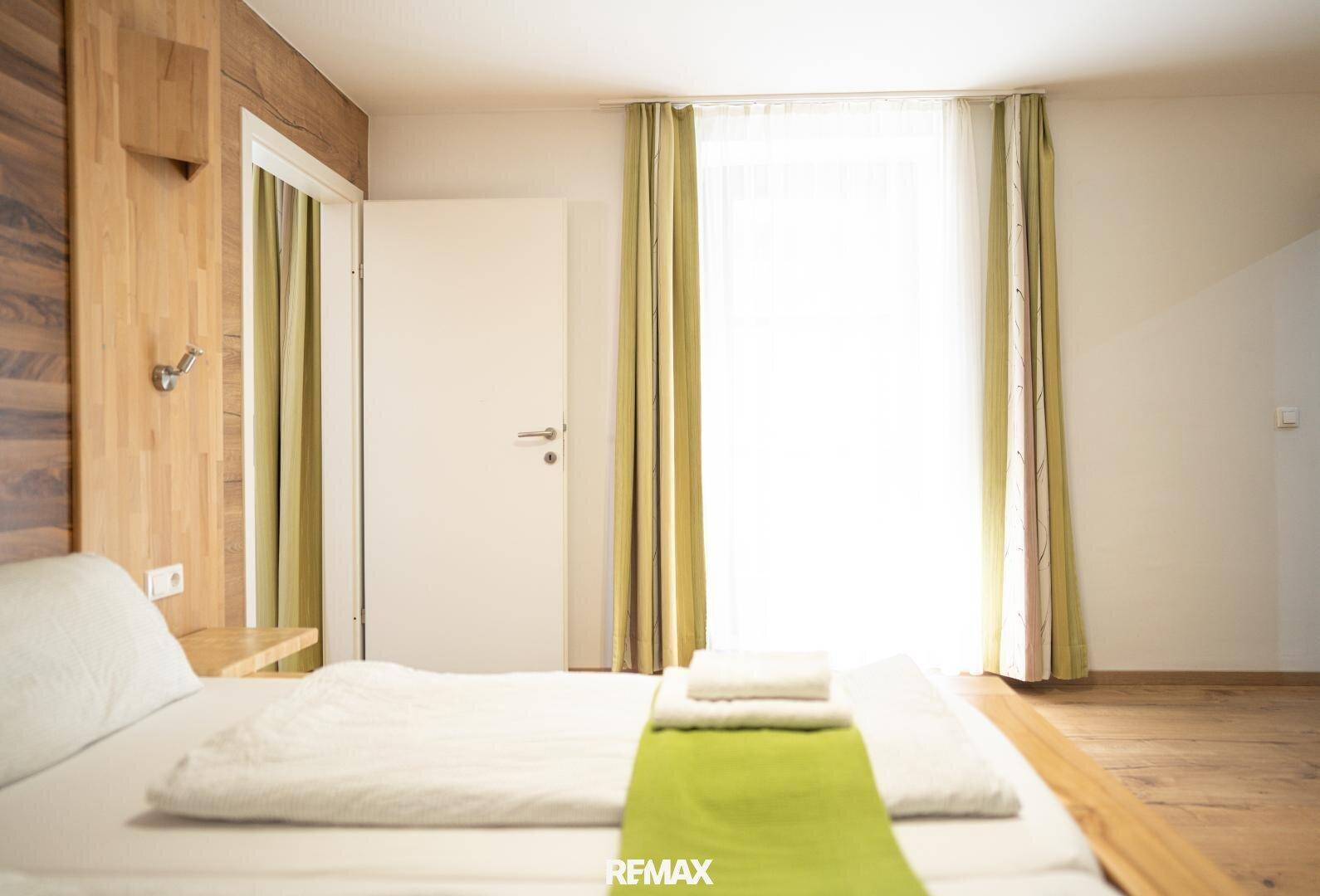 Helles Schlafzimmer mit Holzwandvertäfelung und großem Fenster, das viel Tageslicht hereinlässt.
