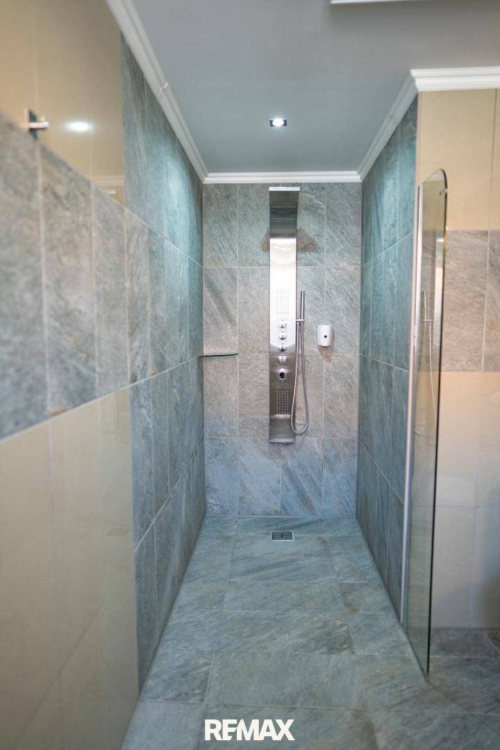 Geräumige begehbare Dusche mit modernen grauen Fliesen und einer Duschsäule.