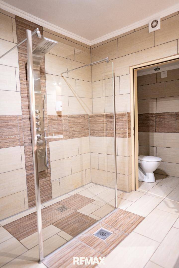 Modernes Badezimmer mit begehbarer Dusche, beigefarbenen Fliesen und Toilette im Hintergrund.
