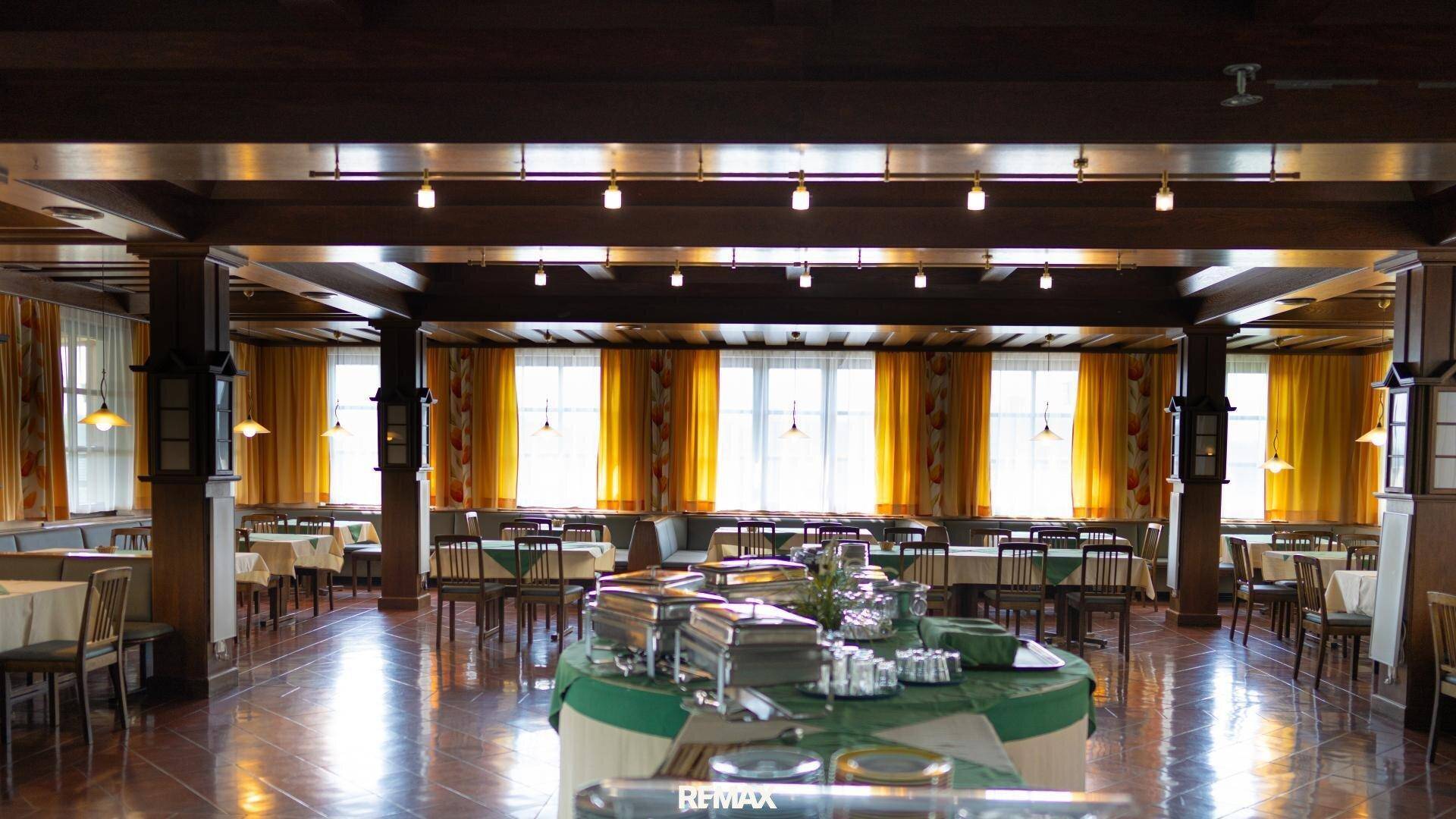 Großer Speisesaal oder Veranstaltungsraum mit vielen Tischen, dunklem Holz und Buffetbereich.