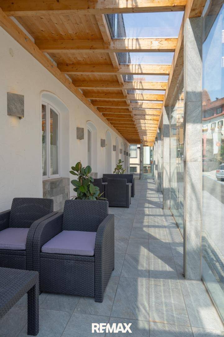 Überdachte Außenterrasse mit Sitzgelegenheiten, Glaswand und Holzbalken, ideal für entspannte Stunden.